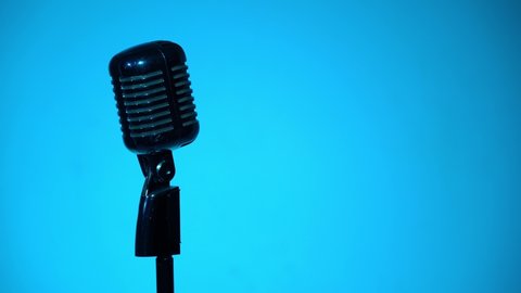 The blue spotlight turns on and illuminates the chrome mic on dark background. Professional concert vintage glare microphone for record or speak to audience on stage in empty retro club close up.