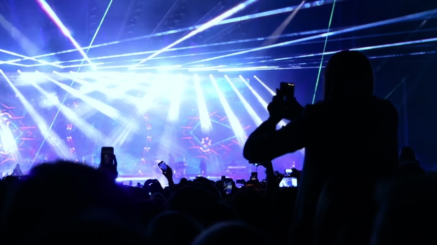 Girl at concert seating on shoulders and raising her hands. Laser show on live music concert. Big crowd of people dancing on music festival concert at night, smusic big event applause raising hands. Royalty-Free Stock Footage #1040617493