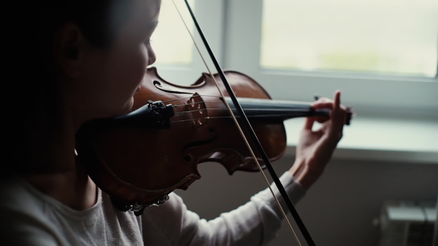 Beautiful girl plays the violin by the window in slow motion Lovely young woman is practicing playing musical instrument at home. Royalty-Free Stock Footage #1040620454