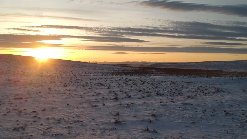 Winter Alberta plains aerial footage at sunset - snowy field and painted clouds shot from a drone