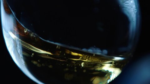 Waving gold white wine in a glass on dark background . Beautiful stock footage for wine commercial . Close up video of wine mixing process inside goblet . Shot on ARRI ALEXA in Slow Motion .