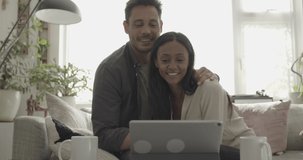 Couple embracing on sofa on video call using digital tablet