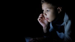 Little boy playing on laptop at the game at night in the dark. Surprised child looks at the computer screen.
