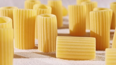 Italian pasta called mezzi rigatoni on white cotton cloth ,tube-shaped pasta with ridges down their lenght , racking focus 