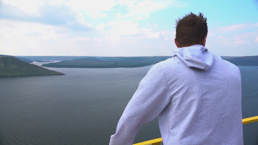 Alone bearded man staying on border edge of carrier filled water river dam