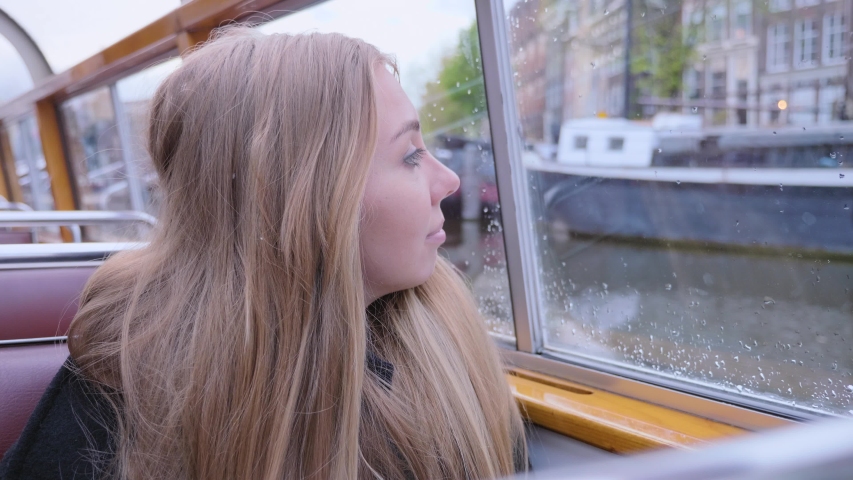 Beautiful lady sitting in cruise boat along canals in Amsterdam. Tourism in the Netherlands. European trip, destination, adventure concept.Pretty blonde girl travelling alone in a ship,looking around