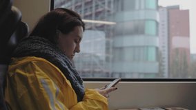 woman sitting in a moving train by the window and looking at her phone. woman in yellow raincoat. 4k video. 59.94 fps