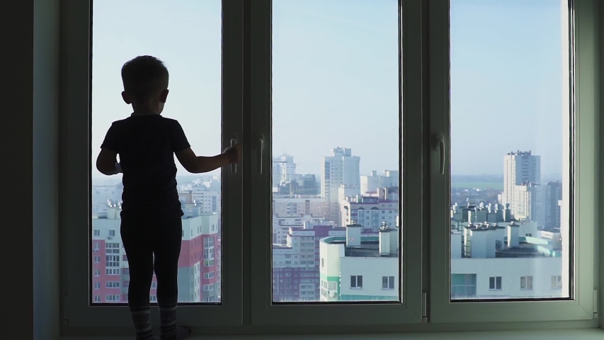 Silhouette of a little boy standing by window against the background of a big city with skyscrapers