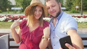 Young couple taking a selfie portrait while relaxing in a city park. Happy lovers want to capture a pleasant moment. Slow motion