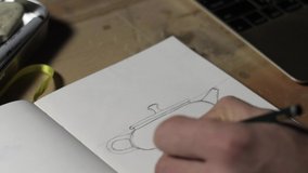 Close-up of a male hand drawing a clay teapot sketch on paper. Male hand draws with a pencil. Macro view. 4k video. 59.94 fps