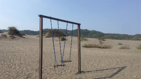 The old rope wooden swing on the desert or sandy beach with mountain background