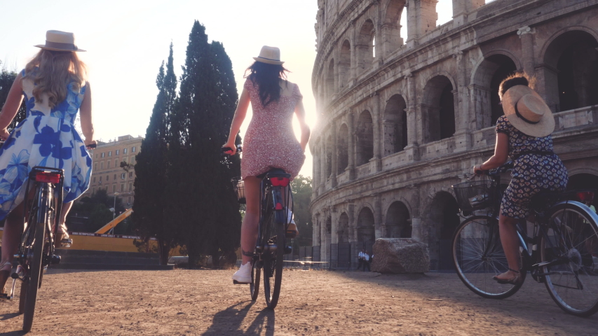 Three happy young women friends tourists riding bikes at Colosseum in Rome, Italy at sunrise. Royalty-Free Stock Footage #1040681756