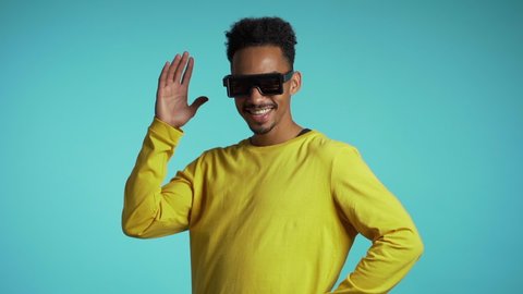 Mixed race man in glowing glasses dancing on blue studio background. Night club, party, positive lifestyle concept. Slow motion.
