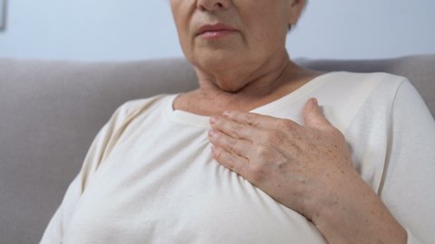 Mature lady hardly breathing and holding hand on chest. risk of heart attack.