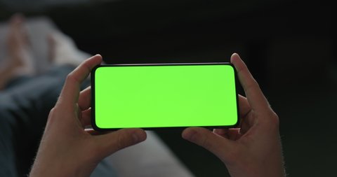 Slow motion man hold smartphone with green screen while lying on a couch
