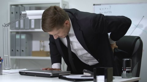 Male boss finishing work on laptop and standing up then feeling strong pain in back.