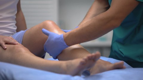 Doctor in gloves examining painful knee of female patient leg trauma.healthcare