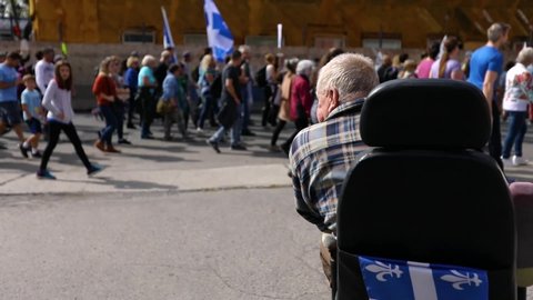 A disabled elderly man in a wheelchair viewed from the back watches marchers pass by at an environment demonstration in French Canadian City