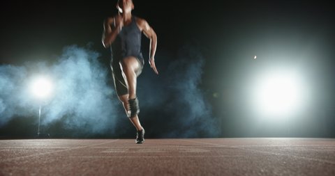 An asian male athlete is sprinting on stadium track during his evening training, spotted on smoked black background -sports concept 4k footage