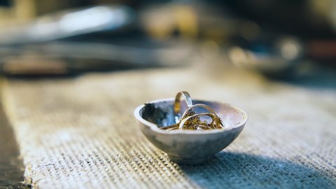 CU: old gold rings melt in small crucible with torch flame on table with asbestos sheet in jewelry workshop closeup