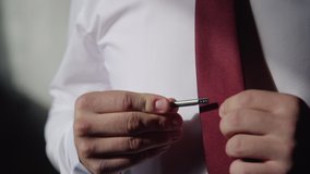 Young groom straightens tie. fiance adjusts his tie clip before the wedding. business man putting clip on the red tie. elegant, suit, event, formal, male, hands concept