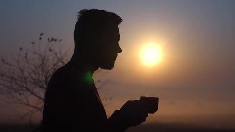 Young bearded guy drinking coffee at dawn. Fragrant coffee in the morning at sunrise. The guy enjoys coffee.The average plan