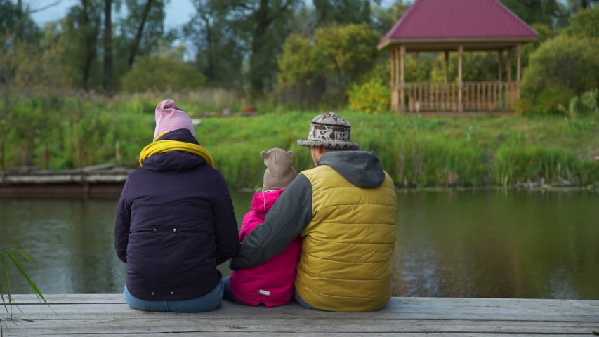 Rear View of Young Family Sitting on Pier in Autumn Day. They Enjoying Nature and Time Together. Family, Leisure and People Concept