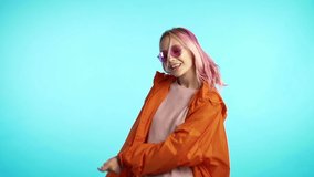 Funny unusual woman with pink hair having fun, smiling, dancing in studio against blue background. Music, dance concept, slow motion