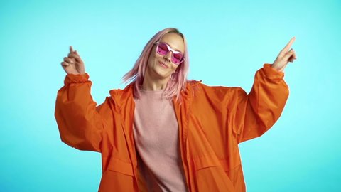 Funny unusual woman with pink hair having fun, smiling, dancing in studio against blue background. Music, dance concept, slow motion