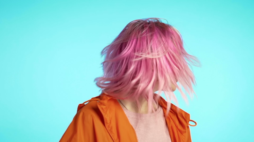 Girl moves to rhythm of music. Woman with colorful hairstyle dancing on blue background. Female having fun. She smiling, hair flutter beautifully. Amazing positive footage.