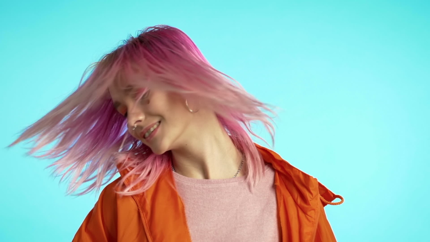 Girl moves to rhythm of music. Woman with colorful hairstyle dancing on blue background. Female having fun. She smiling, hair flutter beautifully. Amazing positive footage.