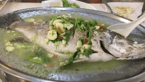 Video of hot steamed fish with spicy green chili and hot soup served on stainless steel tray in a seafood restaurant. Chinese and Asian food menu concept