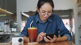 Young Asian woman using smartphone drinking ice tea in cafe chatting with friends. Girl using cellphone in coffee shop.