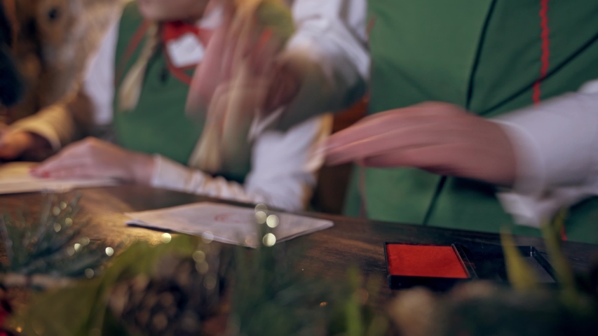 Envelopes on the table for Christmas. Fairy elf puts seal on envelopes. Quick motion. Close-up hands with signet.