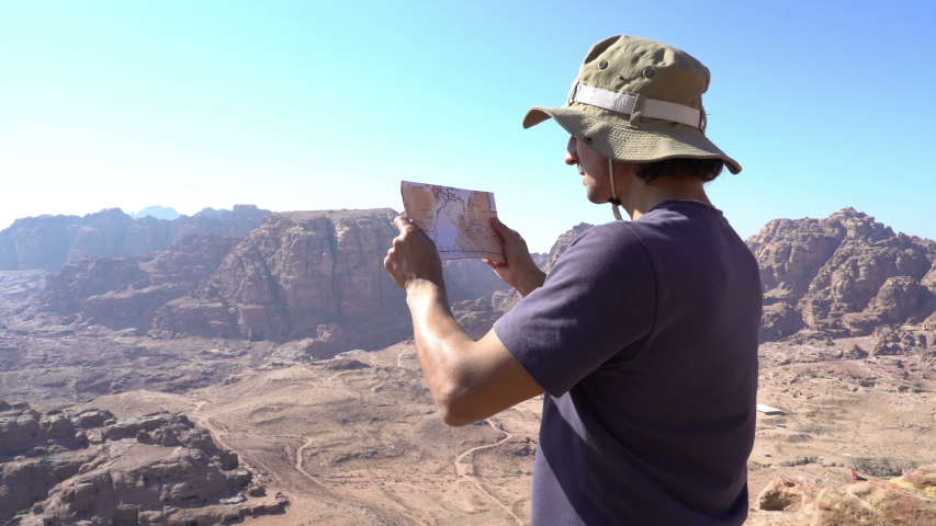 Man with map standing at the edge of mountains and looking around