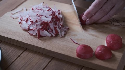 A Housewife slices red radish on a cutting board, close up chop radishes