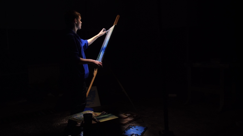Artist copyist paint seascape with ship in ocean. Craftsman decorator draw as boat sail on blue sea with acrylic oil color. Black background. Indoor. Wide angle shot cinematic look.