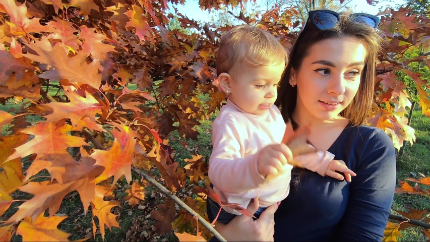 Mother with her little baby girl stand in front of red tree. Autumn park