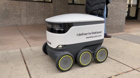 PITTSBURGH, PA - Circa November, 2019 - The Starship delivery robot, an automated delivery service, travels on the sidewalks of Oakland near the PITT campus. Traffic on Forbes Avenue travels along.