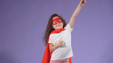 Portrait of beautiful kid with curly hear wearing red cloak and red mask looking side, purple background. Children interested in cosmos