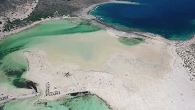 Aerial video view from backside moving drone on Balos lagoon with sandy sea beach with sunbathing and swimming tourists. Dimos Kissamou, Chania prefecture, Crete, Greece.