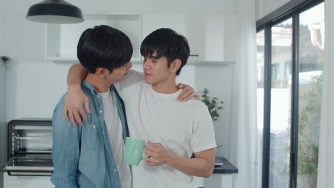 Asian gay couple drinking coffee, having a great time at home. Young handsome LGBTQ+ men talking together spend romantic time in modern kitchen at house in the morning concept.