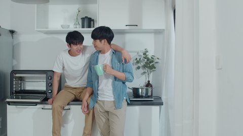 Asian gay couple drinking coffee, having a great time at home. Young handsome LGBTQ+ men talking together spending a romantic time in a modern kitchen at house in the morning concept.