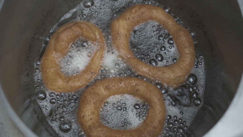Fried doughnut is taken out of a pot of hot vegetable oil. Close-up.