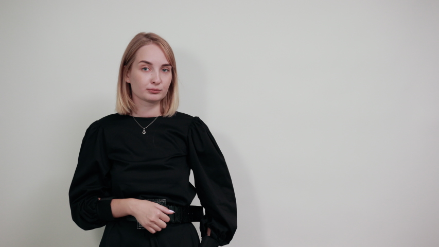 Young woman in black dress looking camera doing phone gesture like says call me back