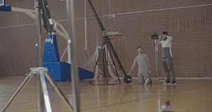 Videographer taking video shots of basketball afro-american man on training in gym. Black guy making slam dunk during game in court. Player wearing unbranded sport clothes. Slow motion 4k raw 60 fps
