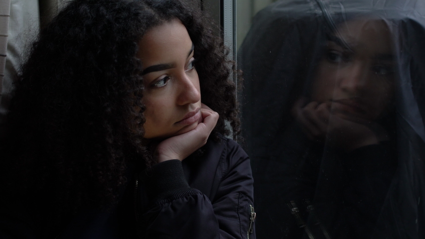 Sad depressed beautiful female mixed race African American girl teenager young woman teen leaning on her hand sitting looking out of a window in self isolation
 | Shutterstock HD Video #1040776235