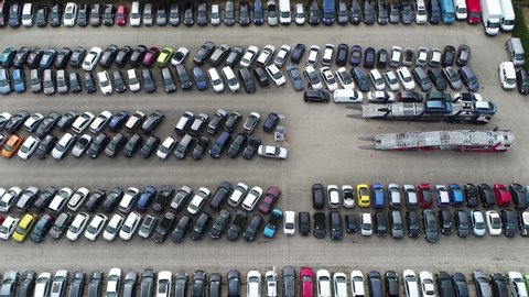 Aerial birds eye view moving towards used car dealership lot showing parked vehicles and automobile offloaded from truck different colored roofs and all vehicle brands 4k high resolution quality