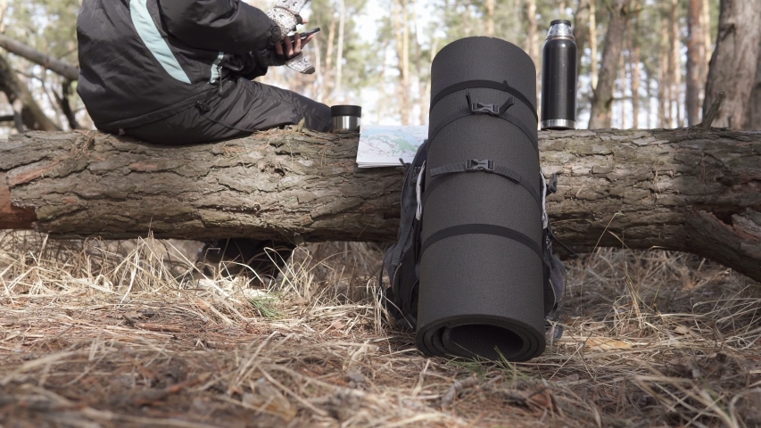Orienteering tourist drinks tea and looks at the map on the phone