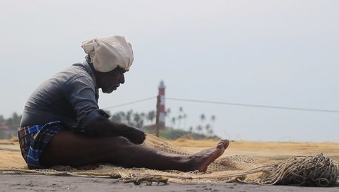Close up shot of the indian fisherman knitting the fishing net at Kovalam beach of Kerala, India: SEP 2019